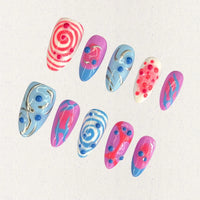 Cosmic Swirls nail set features bold swirls of pink, blue, and white, accented with metallic details and circular 3D elements. This playful yet elegant design mirrors the energetic flow of cosmic waves and nebulae.