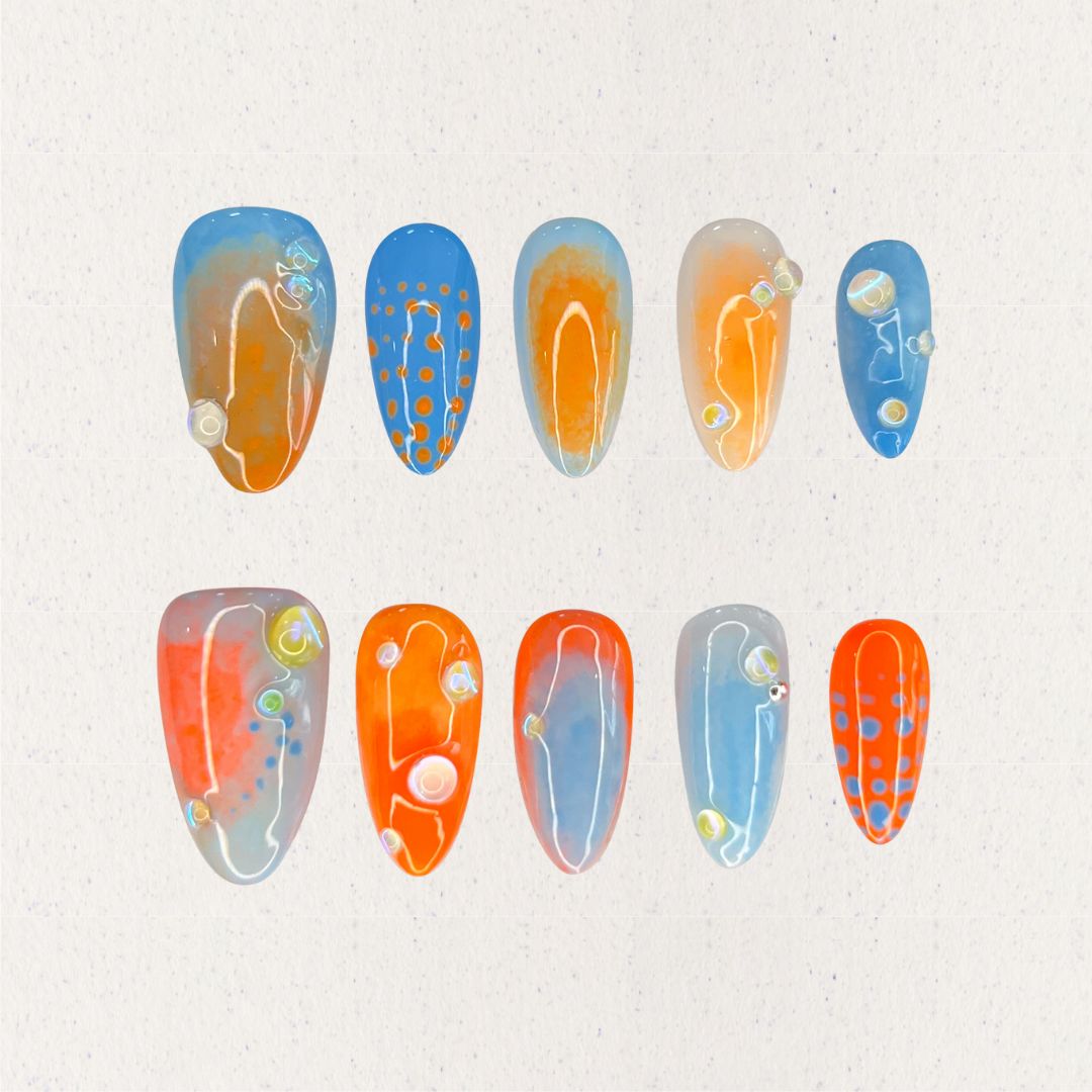 Oceanic Drift nail set includes vivid blue and orange hues with dot designs and glossy finishes, evoking the dynamic movement of the ocean.