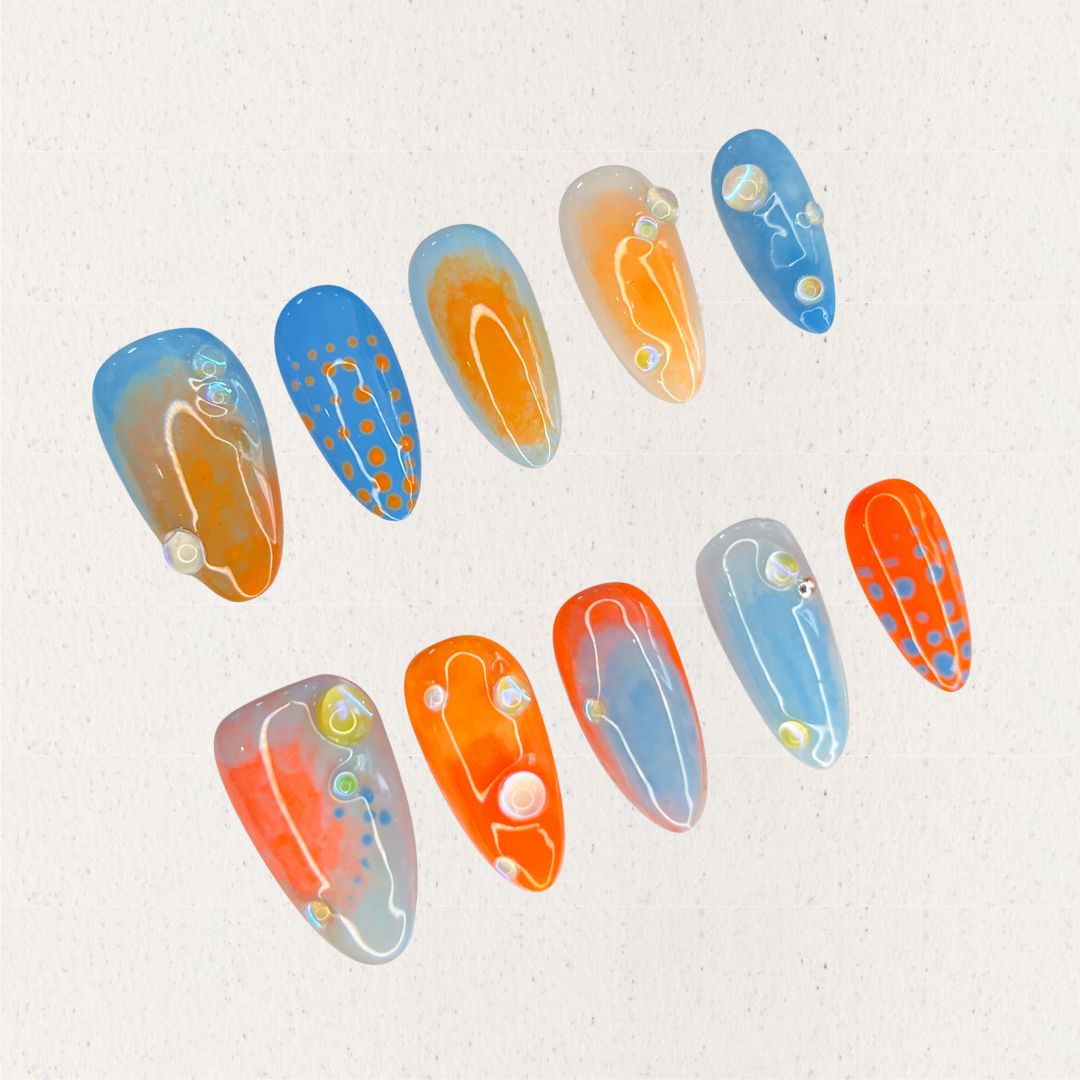 Oceanic Drift nail set includes vivid blue and orange hues with dot designs and glossy finishes, evoking the dynamic movement of the ocean.