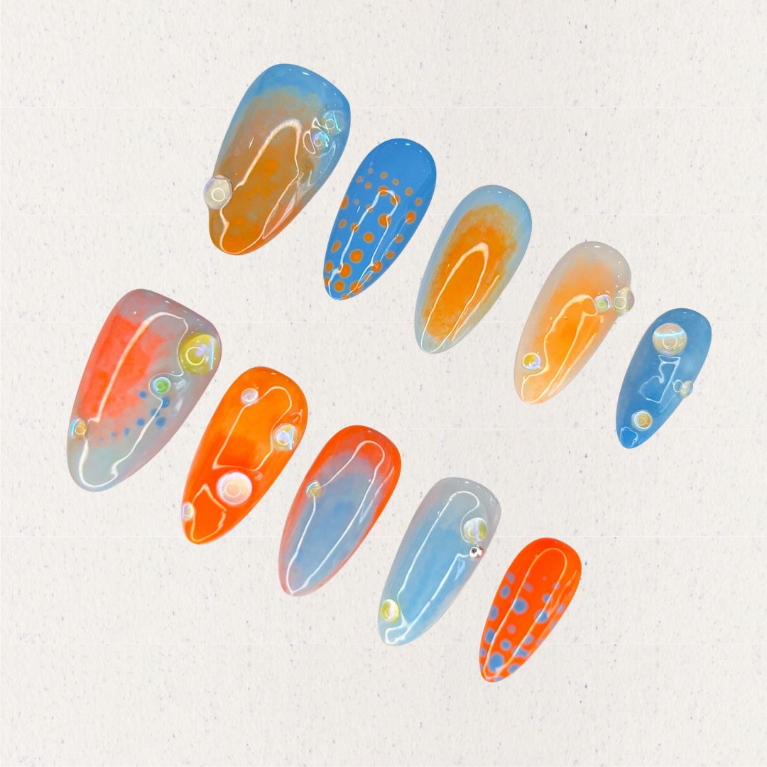 Oceanic Drift nail set includes vivid blue and orange hues with dot designs and glossy finishes, evoking the dynamic movement of the ocean.