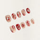 A press-on nail set featuring nude blush gradients with bold red patterns, celestial starbursts, and intricate white accents, creating an ethereal and romantic design.