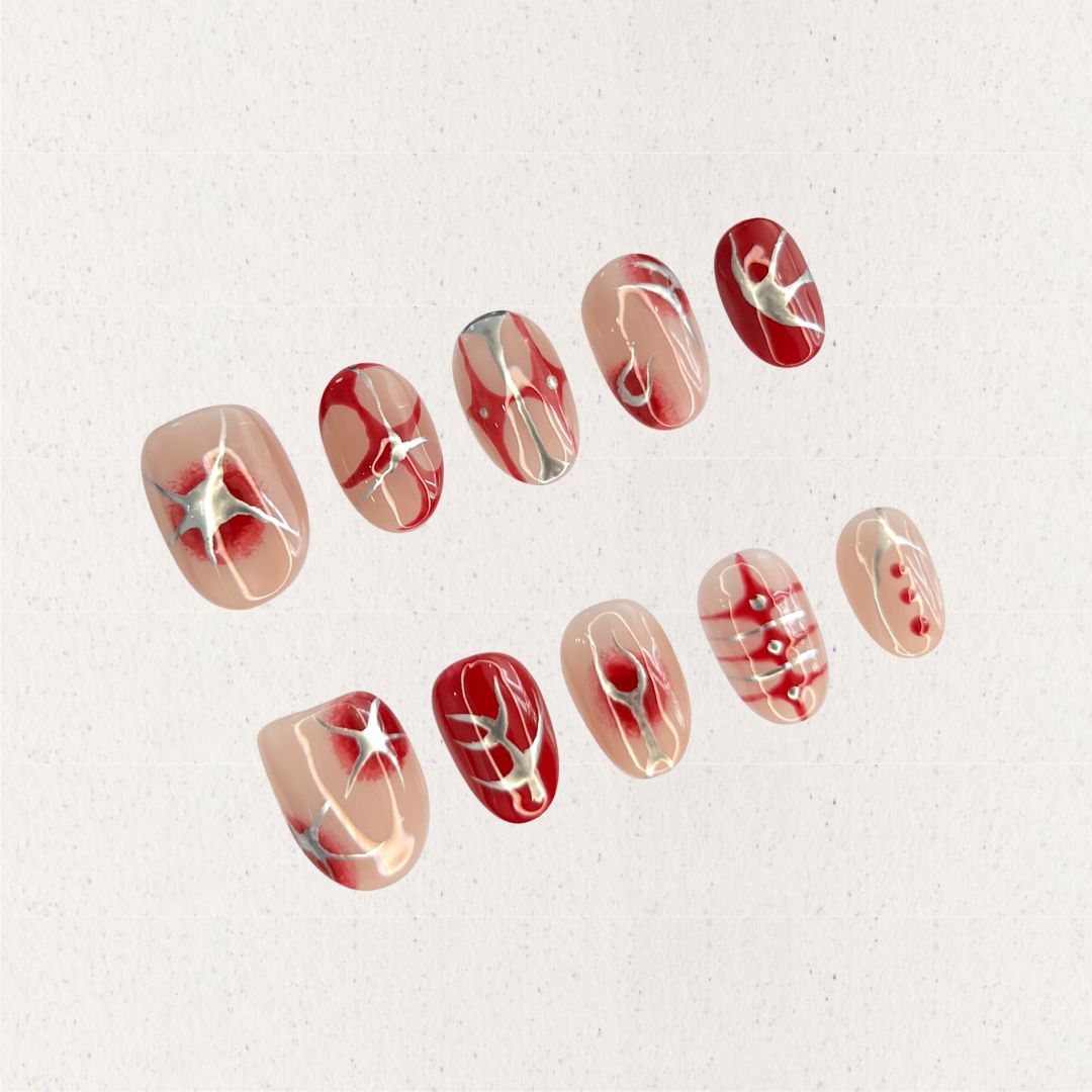 A press-on nail set featuring nude blush gradients with bold red patterns, celestial starbursts, and intricate white accents, creating an ethereal and romantic design.