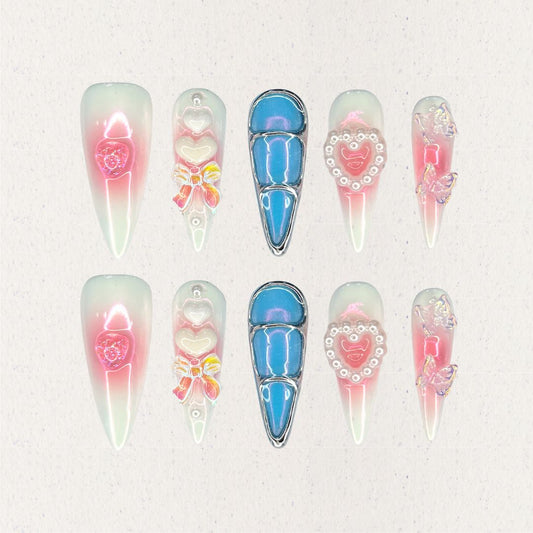 Enchanted Love nail set combines soft pink and white gradients with dazzling blue metallic accents, 3D butterflies, pearls, and heart-shaped embellishments. It creates a whimsical and elegant aesthetic inspired by timeless love stories.