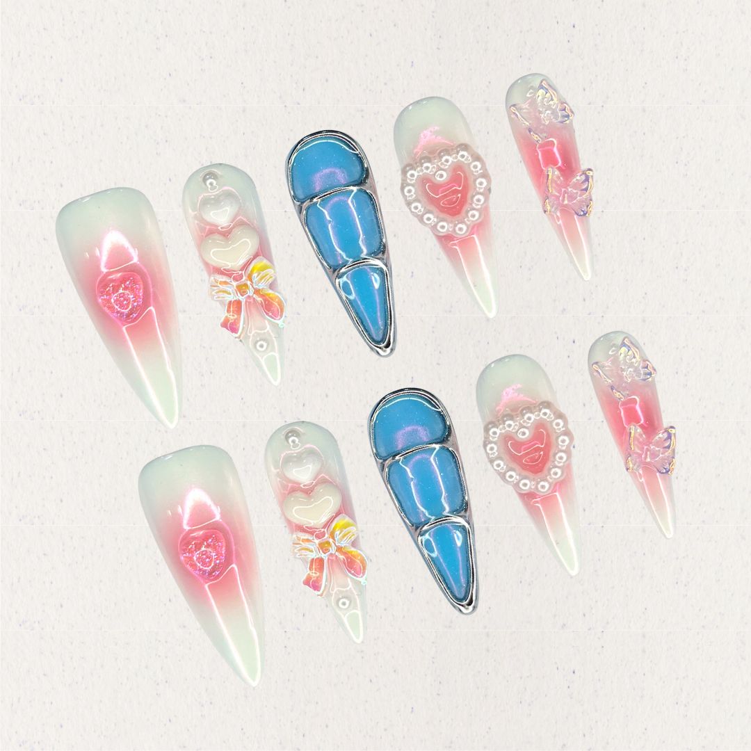 Enchanted Love nail set combines soft pink and white gradients with dazzling blue metallic accents, 3D butterflies, pearls, and heart-shaped embellishments. It creates a whimsical and elegant aesthetic inspired by timeless love stories.