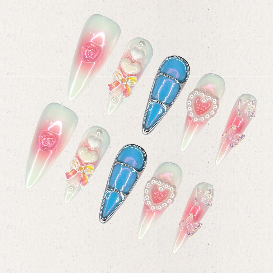 Enchanted Love nail set combines soft pink and white gradients with dazzling blue metallic accents, 3D butterflies, pearls, and heart-shaped embellishments. It creates a whimsical and elegant aesthetic inspired by timeless love stories.