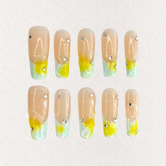 Morning Dew nail set features a subtle nude base with glowing yellow and green gradients, resembling the soft light of early morning. Accented with delicate crystal drops, this design evokes the freshness and purity of dew-drenched flowers at sunrise.