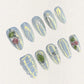 Dewy Berries nail set draws inspiration from dew-kissed berries in a misty meadow. With shimmering blue tones and 3D green and red accents resembling luscious berries, this design celebrates the charm of nature at dawn.
