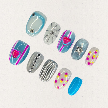 Cosmic Heartbeat nail set combines silver and blue metallic bases with neon pink hearts, sharp star shapes, and polka dot details. This design channels a lively, otherworldly rhythm inspired by cosmic waves and pulsars.