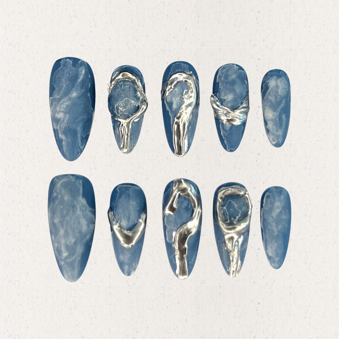 This press-on nail set, titled "Metallic Tide," showcases a deep ocean blue base with delicate marbled textures, resembling swirling water patterns. The standout silver metallic accents create fluid, wave-like designs that mimic flowing liquid metal. The overall aesthetic is modern, minimalist, and artistic, blending nature's elegance with a futuristic touch.