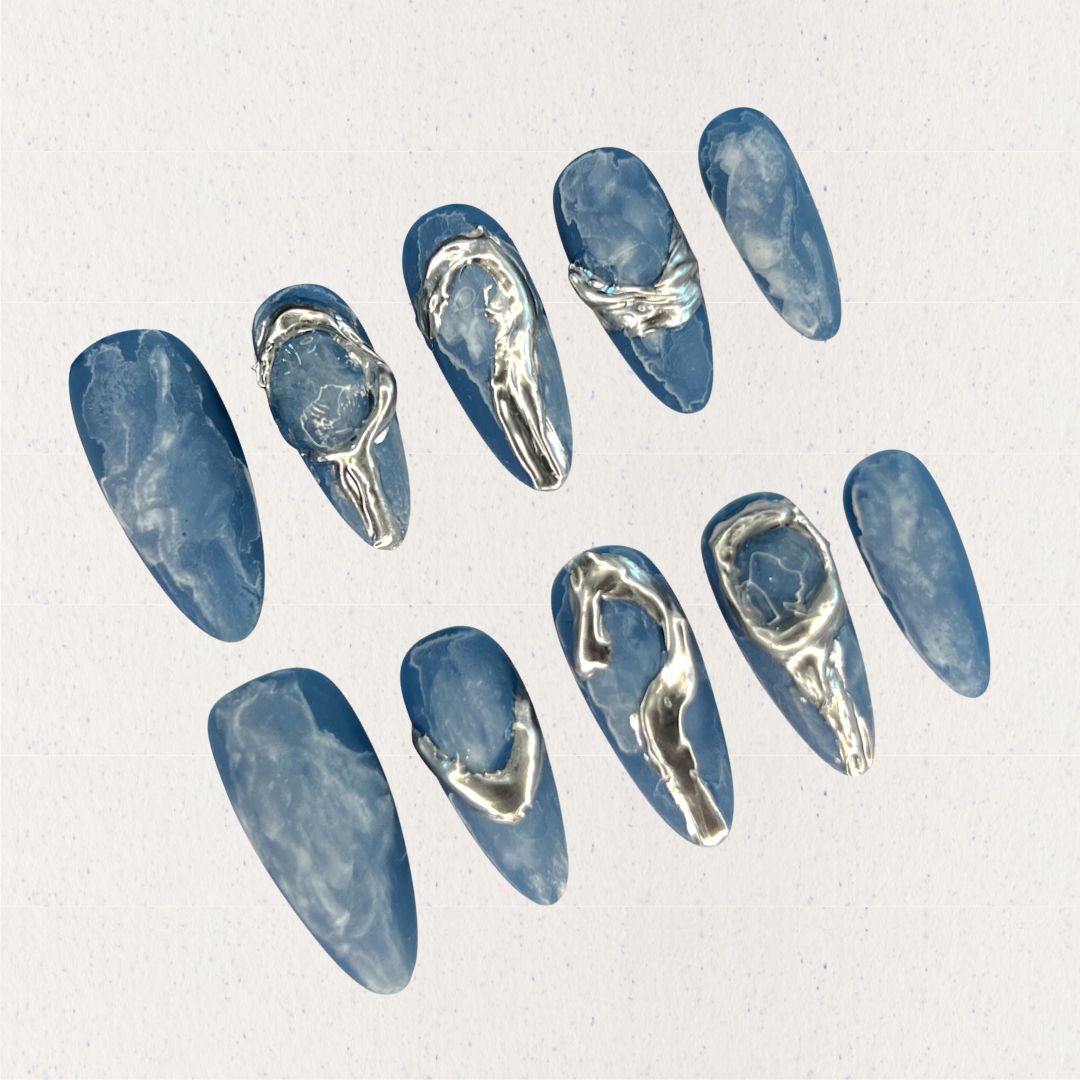 This press-on nail set, titled "Metallic Tide," showcases a deep ocean blue base with delicate marbled textures, resembling swirling water patterns. The standout silver metallic accents create fluid, wave-like designs that mimic flowing liquid metal. The overall aesthetic is modern, minimalist, and artistic, blending nature's elegance with a futuristic touch.