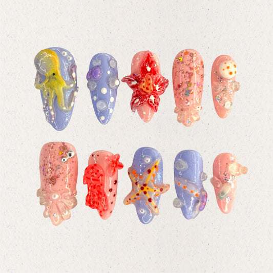 Ocean Realm nail set features vibrant sea-inspired designs, including octopuses, starfish, and jellyfish in vivid reds, blues, and purples. Enhanced with glitter and 3D details, this set celebrates the wonder of marine ecosystems.