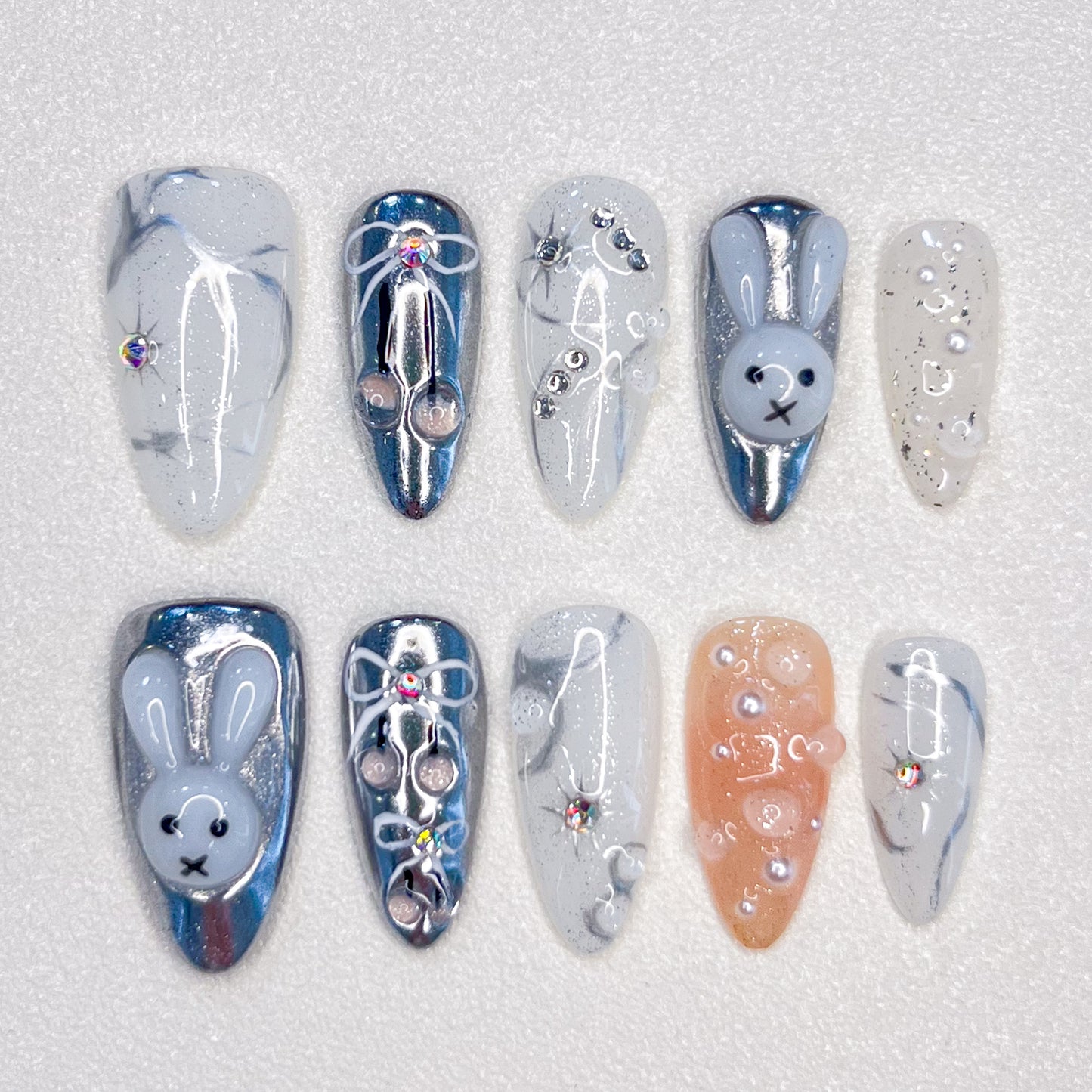 Moonlit Bunny nail set highlights 3D bunny motifs, silver tones, and pearl accents, creating a whimsical yet elegant design under a moonlit glow.