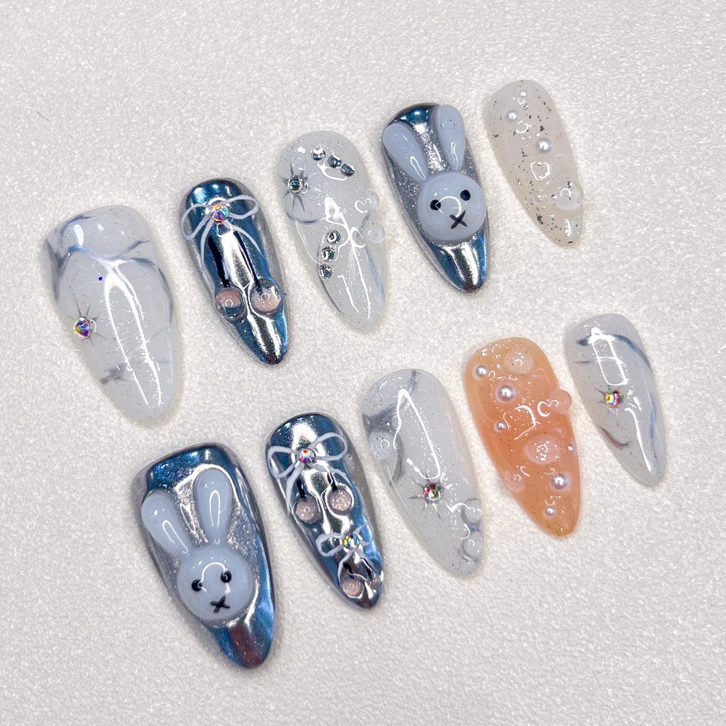 Moonlit Bunny nail set highlights 3D bunny motifs, silver tones, and pearl accents, creating a whimsical yet elegant design under a moonlit glow.