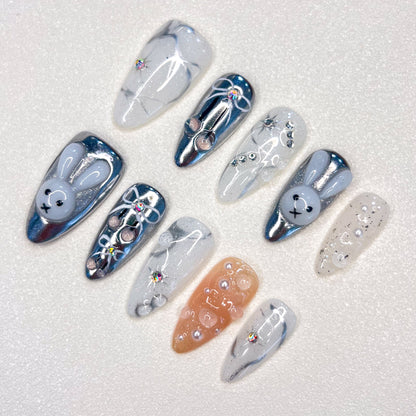 Moonlit Bunny nail set highlights 3D bunny motifs, silver tones, and pearl accents, creating a whimsical yet elegant design under a moonlit glow.