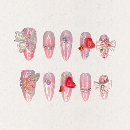 Angelic Grace nail set features shimmering pink hues paired with 3D butterfly wings, intricate ribbons, and vibrant heart accents. This design evokes the elegance of angelic beings, capturing a sense of ethereal beauty and charm.