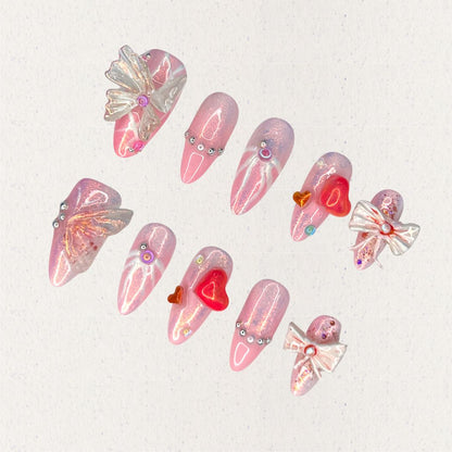 Angelic Grace nail set features shimmering pink hues paired with 3D butterfly wings, intricate ribbons, and vibrant heart accents. This design evokes the elegance of angelic beings, capturing a sense of ethereal beauty and charm.