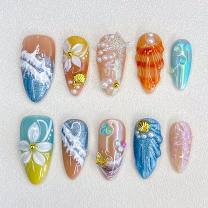 A lively set of press-on nails adorned with multicolored seashells, pearls, and wave motifs, evoking the beauty and mystery of a coral reef.