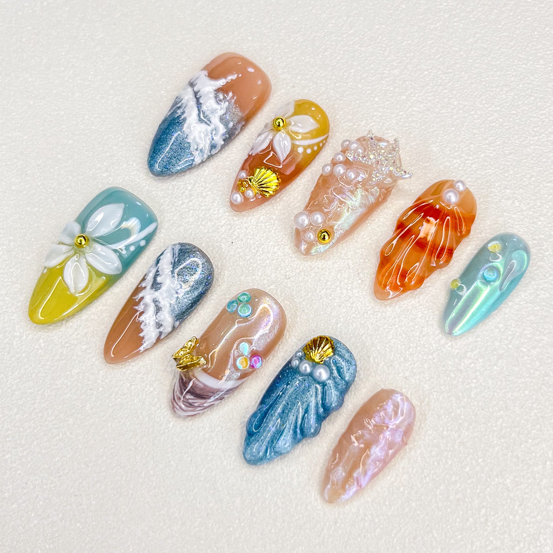 A lively set of press-on nails adorned with multicolored seashells, pearls, and wave motifs, evoking the beauty and mystery of a coral reef.