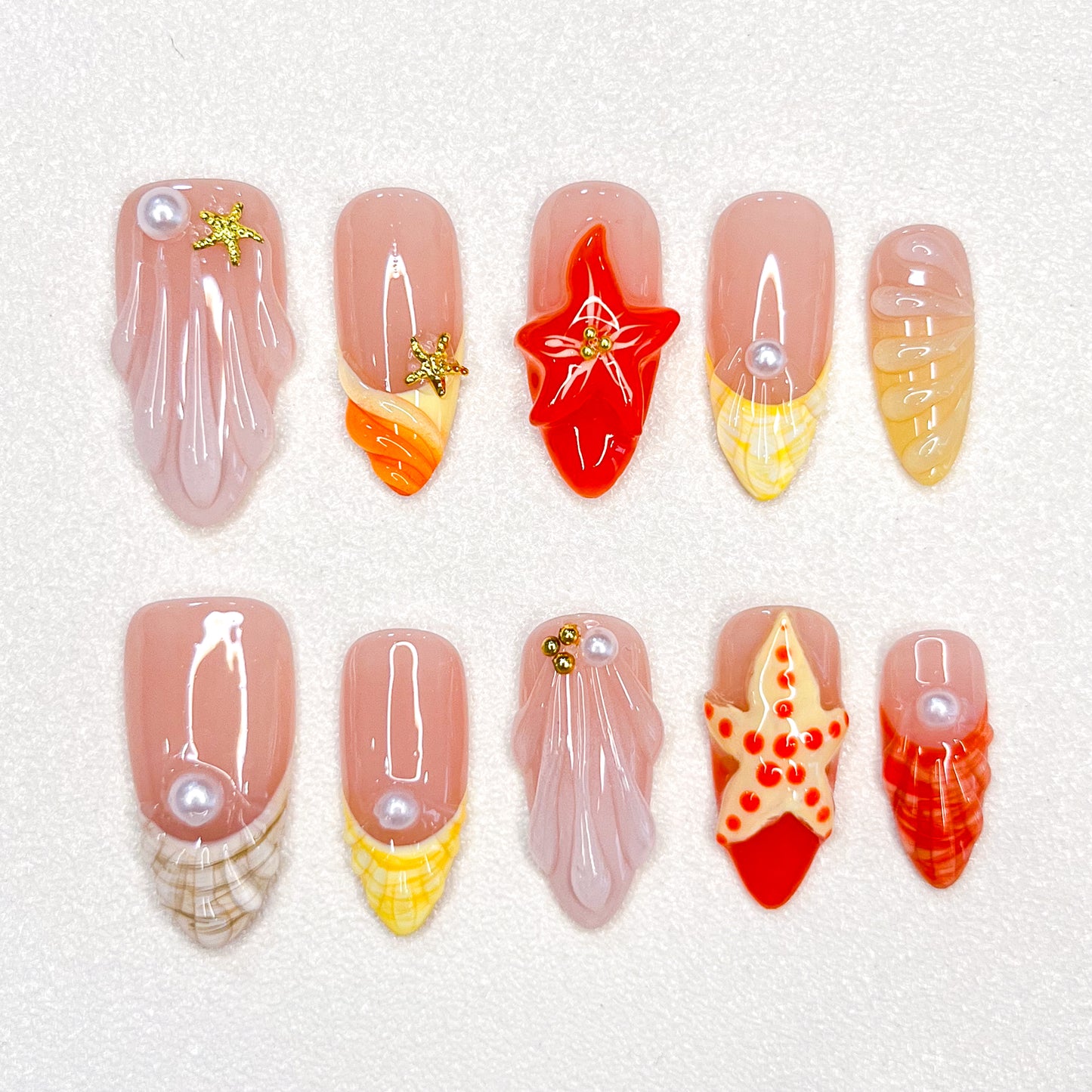 A delicate press-on nail set with a pink base, adorned with seashells, starfish, and pearl details, creating a serene, beach-inspired style that’s both elegant and refreshing.