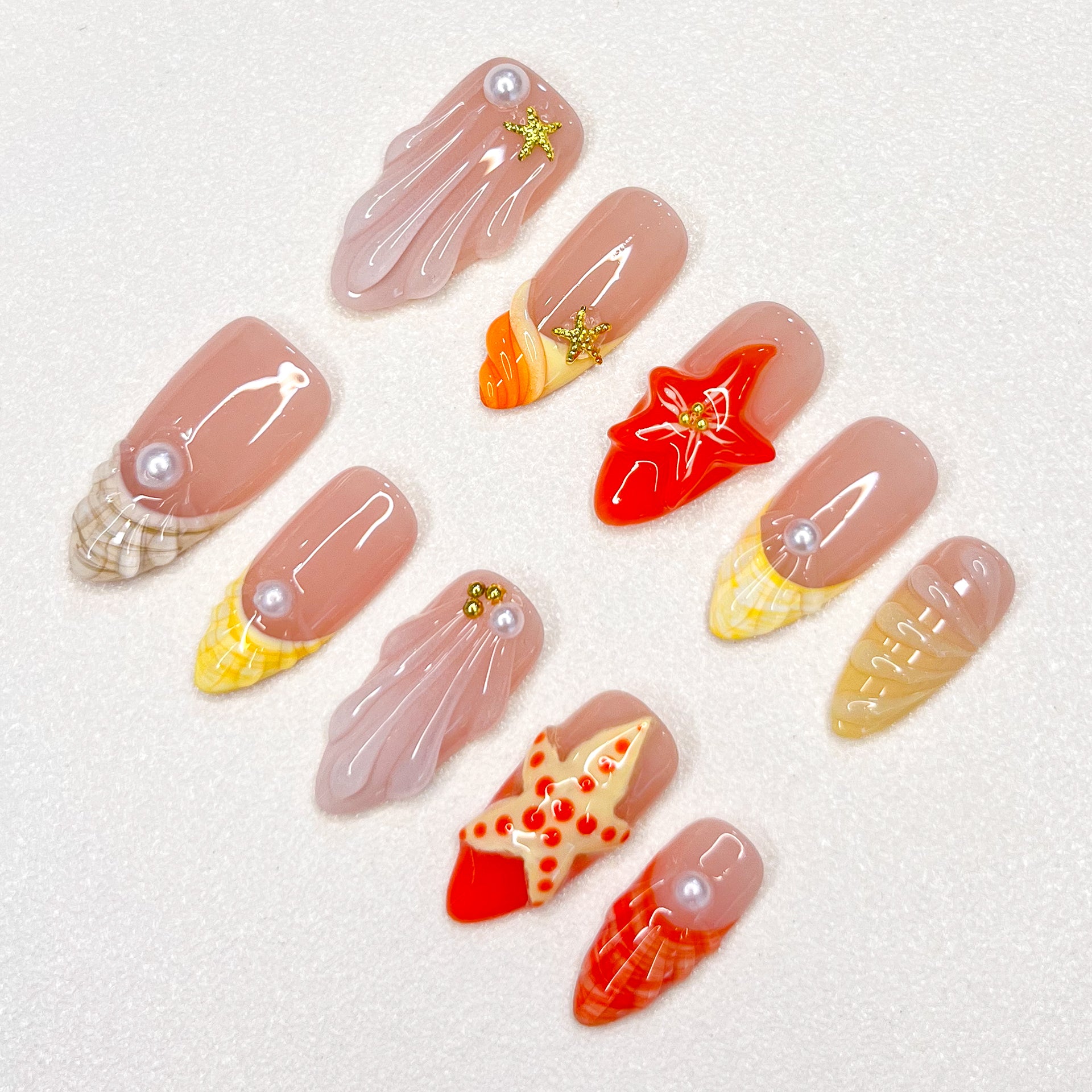 A delicate press-on nail set with a pink base, adorned with seashells, starfish, and pearl details, creating a serene, beach-inspired style that’s both elegant and refreshing.