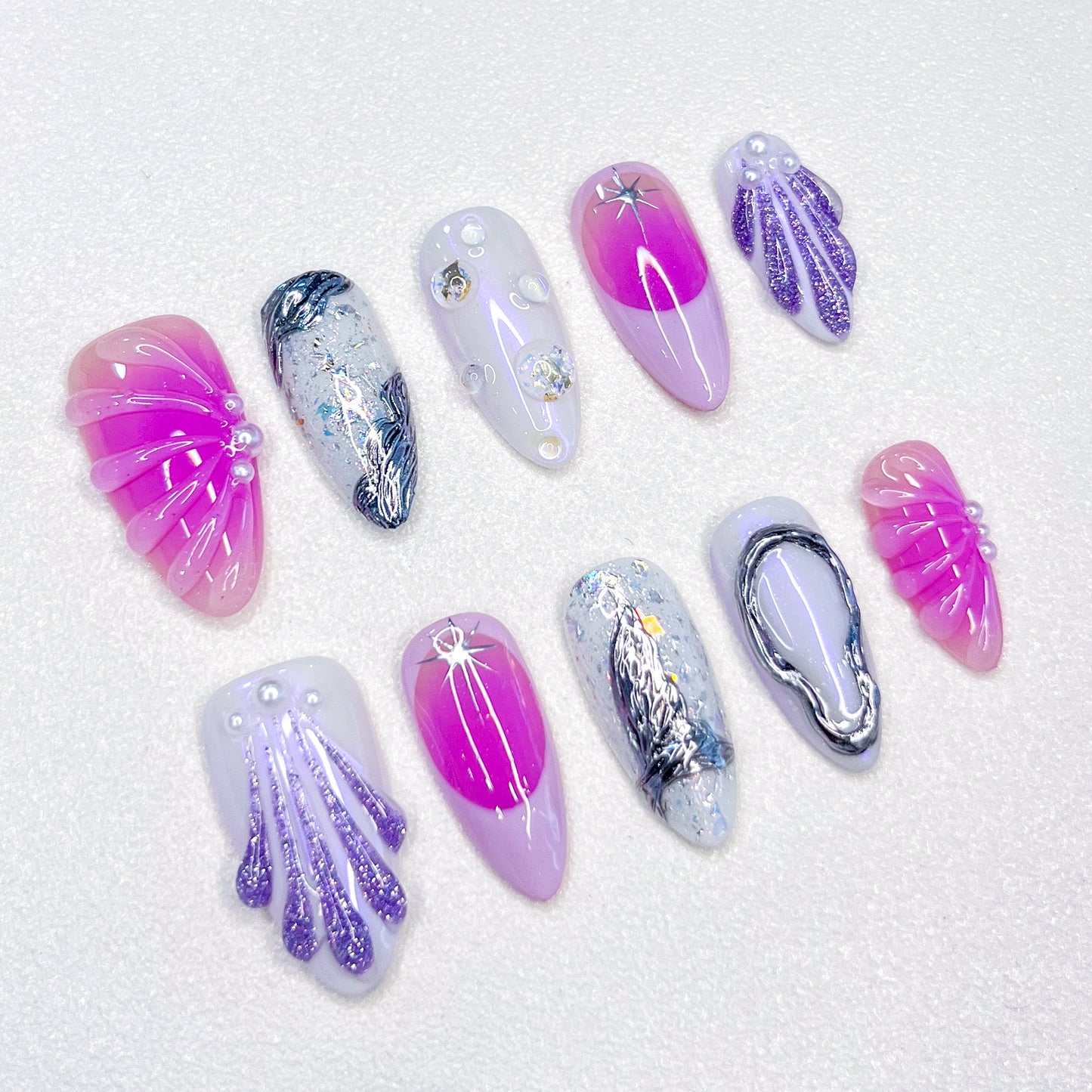 A colorful press-on nail set with purple, rose pink, and blue tones, adorned with seashells and wave designs, bringing a dreamy, mermaid-inspired charm to your style.