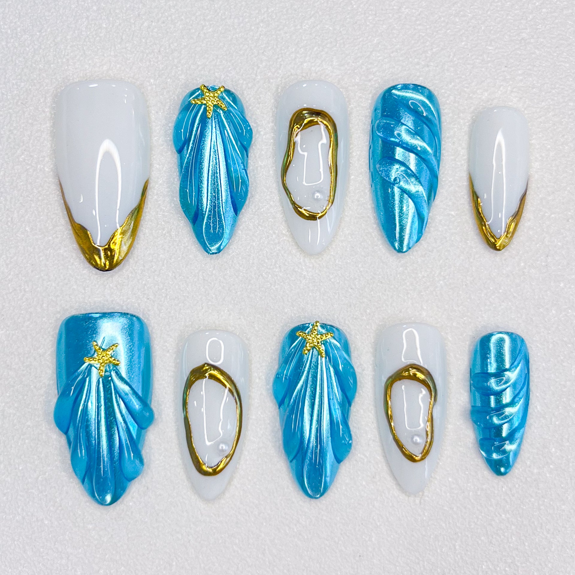 Ocean Glimmer press-on nails with blue and gold ocean-inspired design, featuring shell shapes and starfish details for a chic, beachy style.