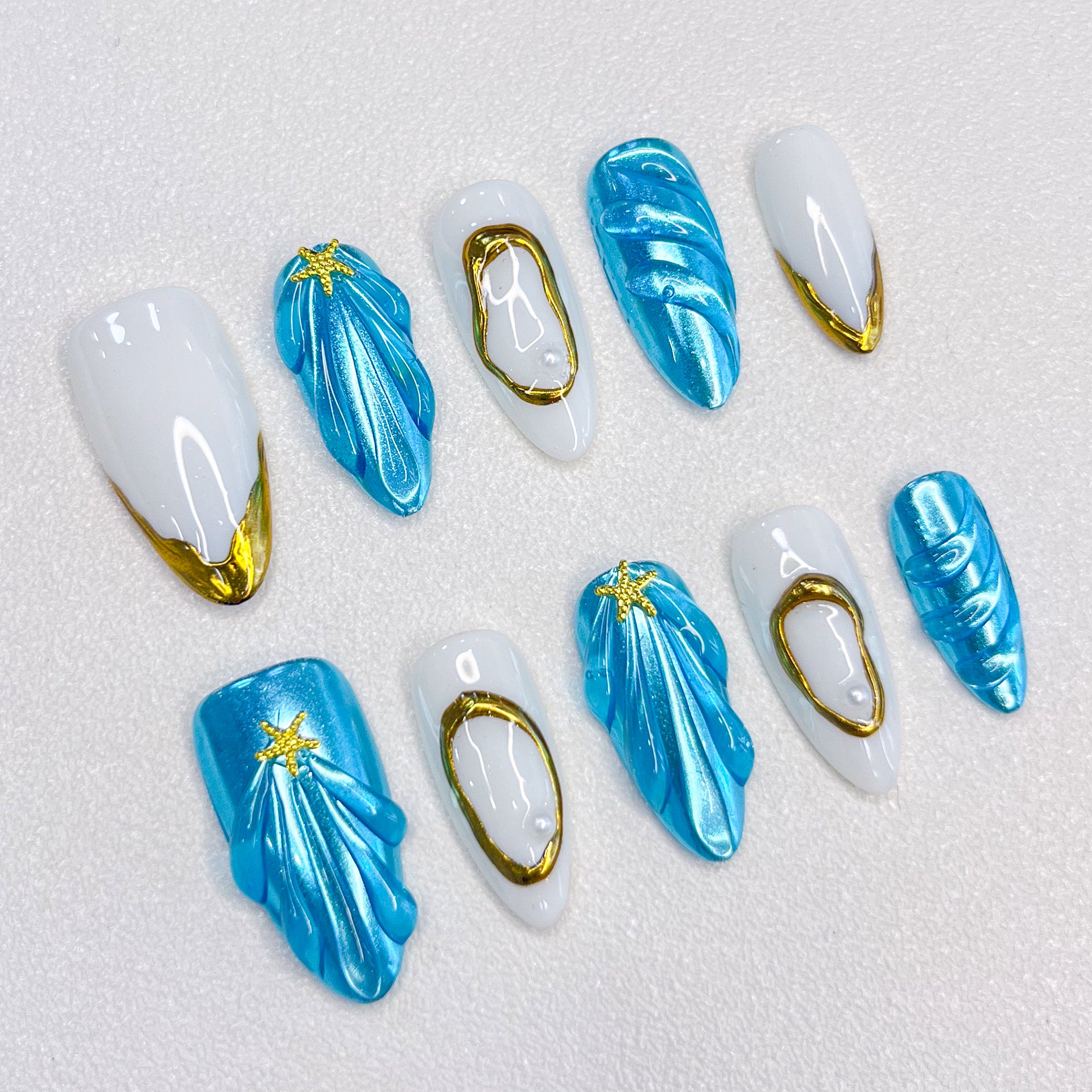 Ocean Glimmer press-on nails with blue and gold ocean-inspired design, featuring shell shapes and starfish details for a chic, beachy style.