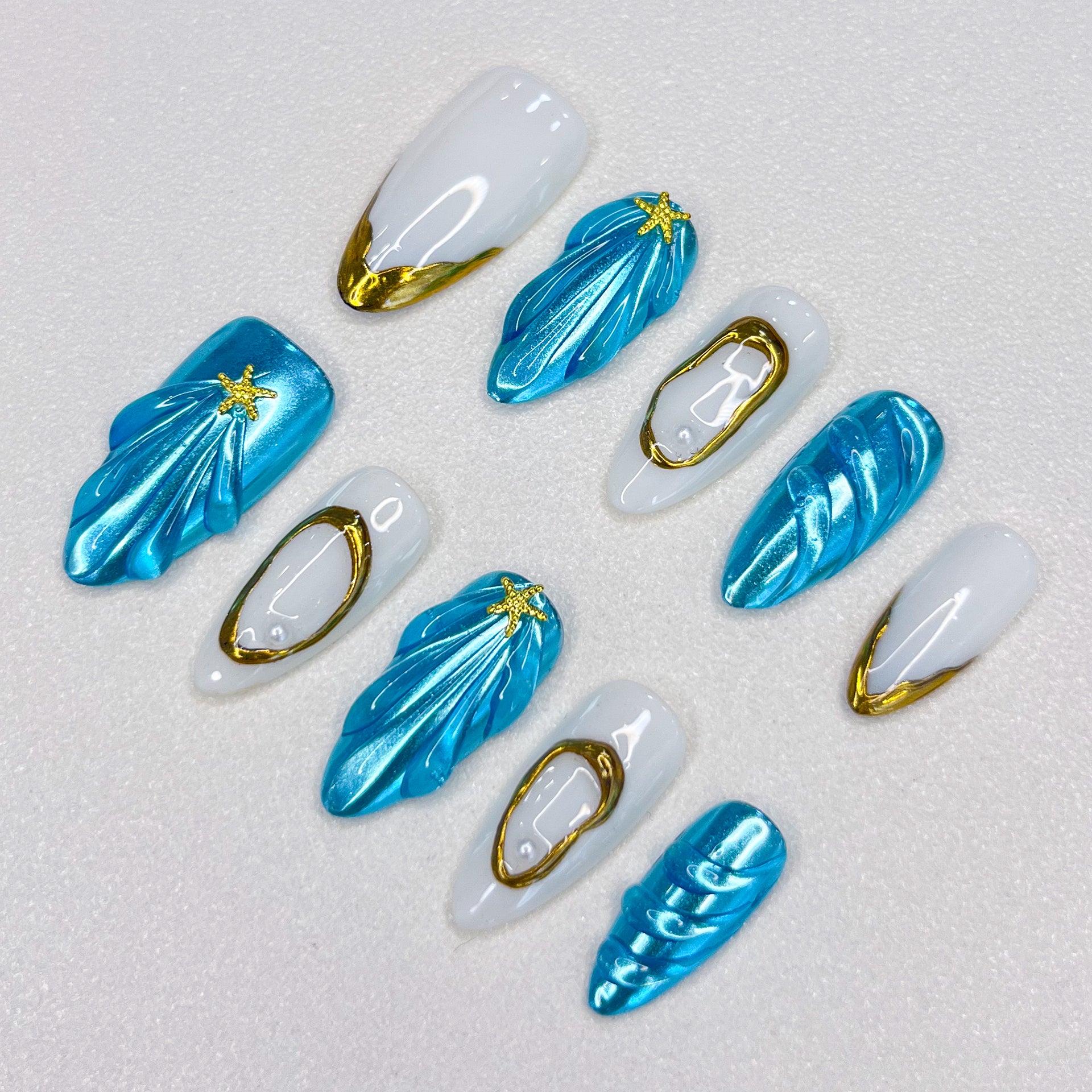 Ocean Glimmer press-on nails with blue and gold ocean-inspired design, featuring shell shapes and starfish details for a chic, beachy style.