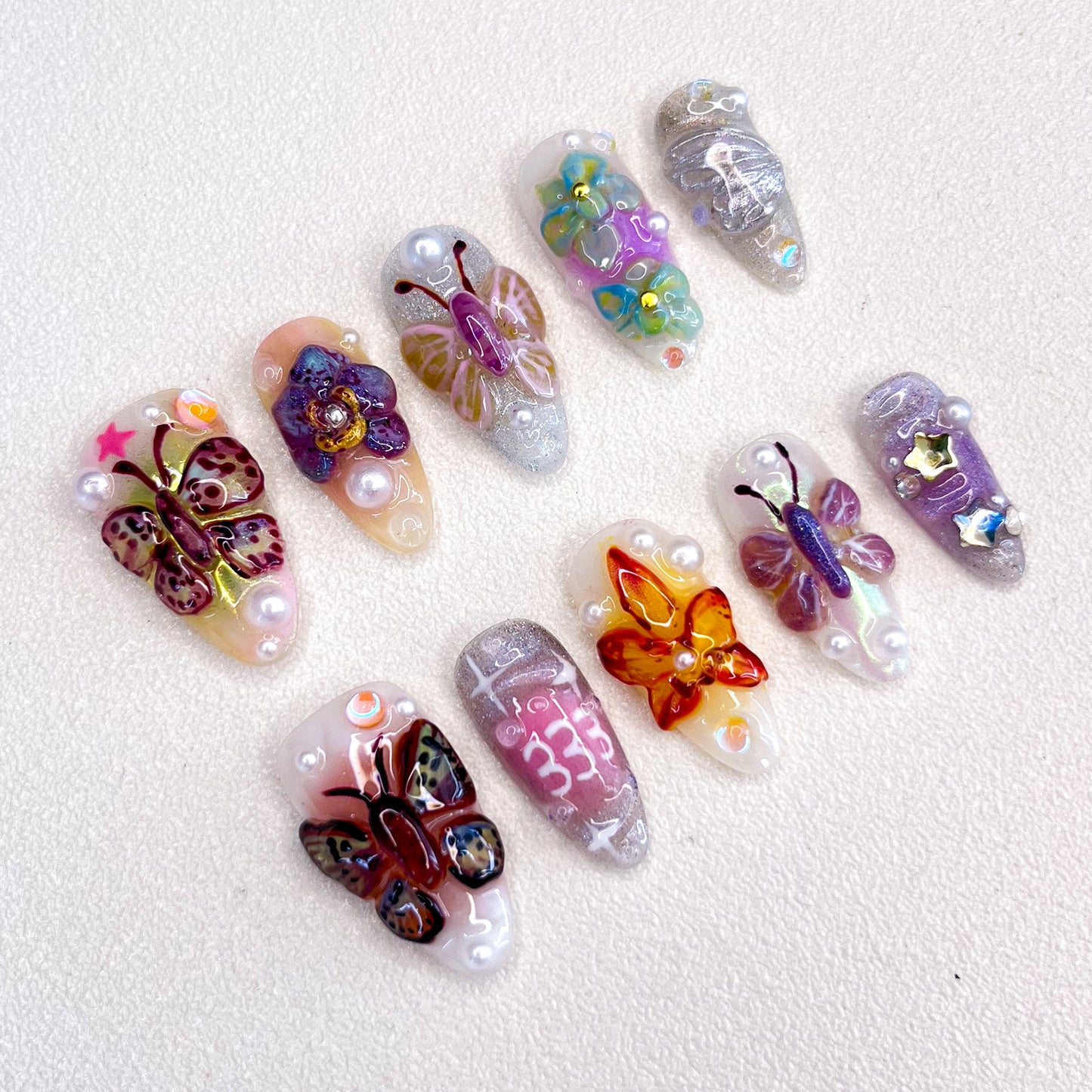 3D nail art featuring vibrant butterflies and flowers with pearl accents on a shimmering base.