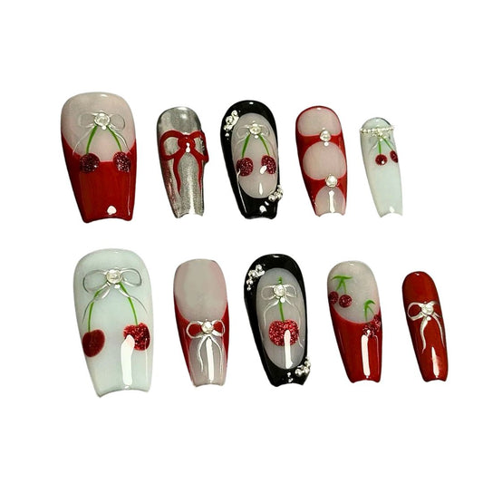 A press-on nail set with cherry patterns, bows, and rhinestone details on red, black, and white bases, offering a blend of playful charm and classic elegance.