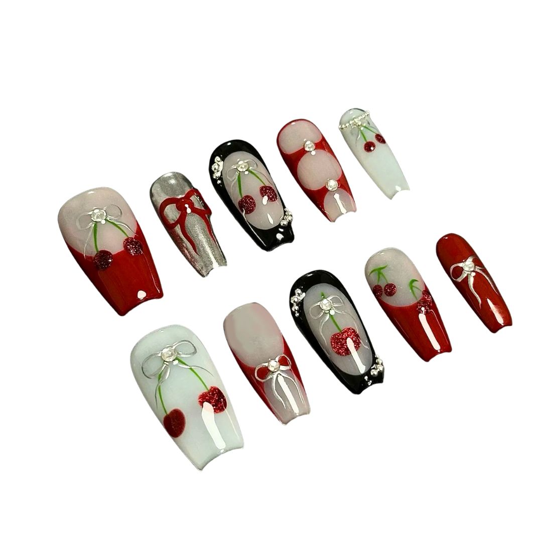 A press-on nail set with cherry patterns, bows, and rhinestone details on red, black, and white bases, offering a blend of playful charm and classic elegance.