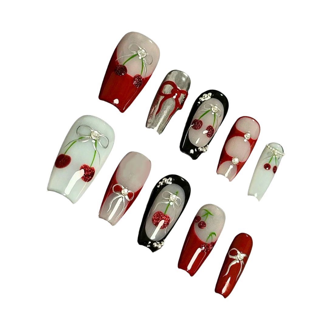 A press-on nail set with cherry patterns, bows, and rhinestone details on red, black, and white bases, offering a blend of playful charm and classic elegance.