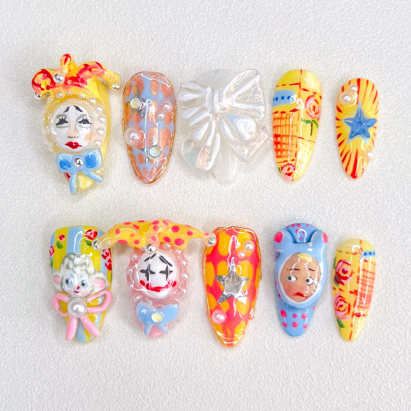 A set of colorful, carnival-inspired press-on nails featuring intricate 3D designs like clowns, bows, stars, and playful hand-painted details in bold hues like red, yellow, and blue.