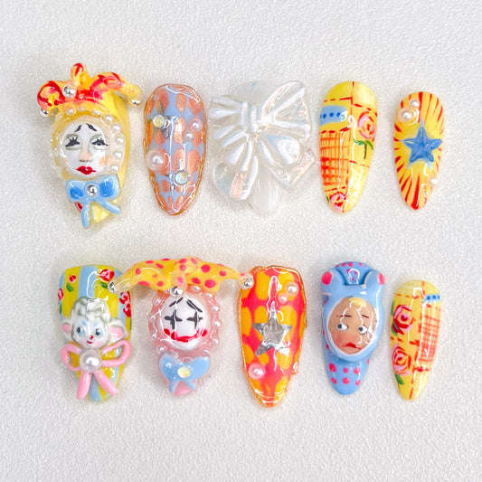 A set of colorful, carnival-inspired press-on nails featuring intricate 3D designs like clowns, bows, stars, and playful hand-painted details in bold hues like red, yellow, and blue.