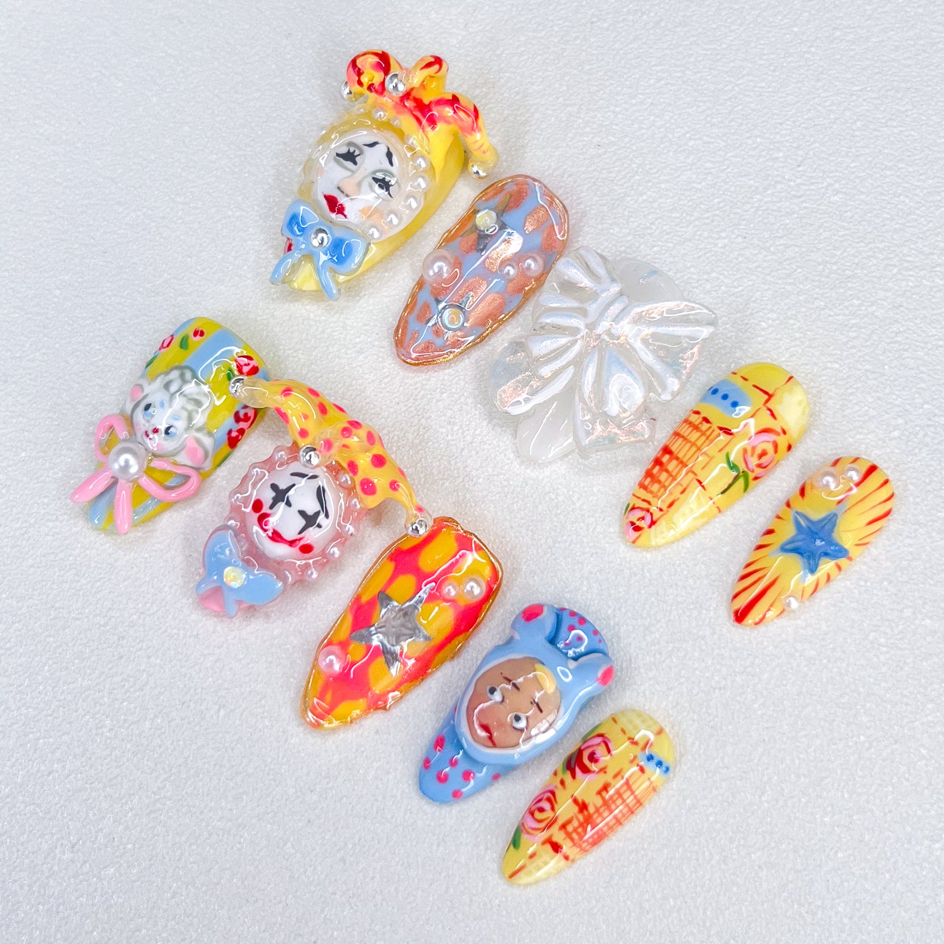 A set of colorful, carnival-inspired press-on nails featuring intricate 3D designs like clowns, bows, stars, and playful hand-painted details in bold hues like red, yellow, and blue.