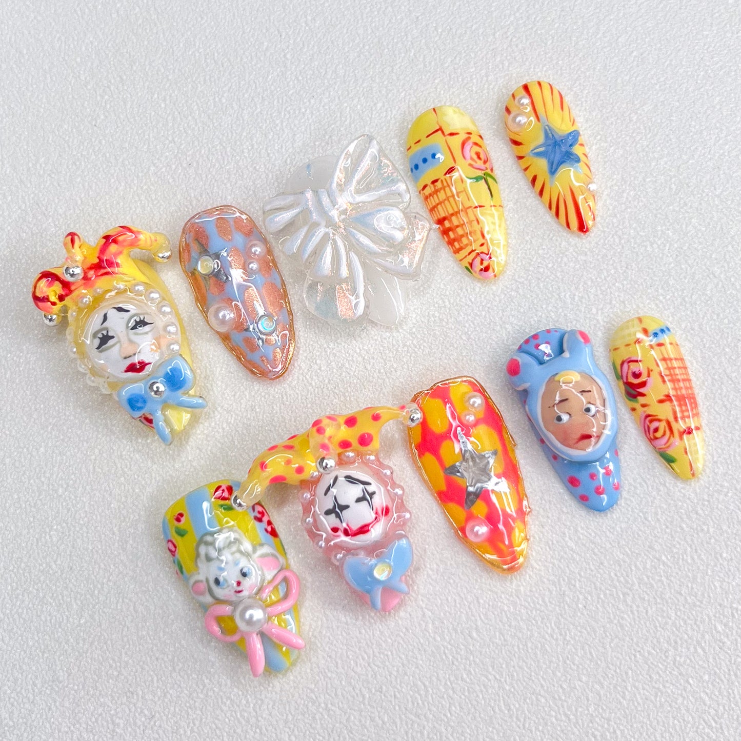 A set of colorful, carnival-inspired press-on nails featuring intricate 3D designs like clowns, bows, stars, and playful hand-painted details in bold hues like red, yellow, and blue.