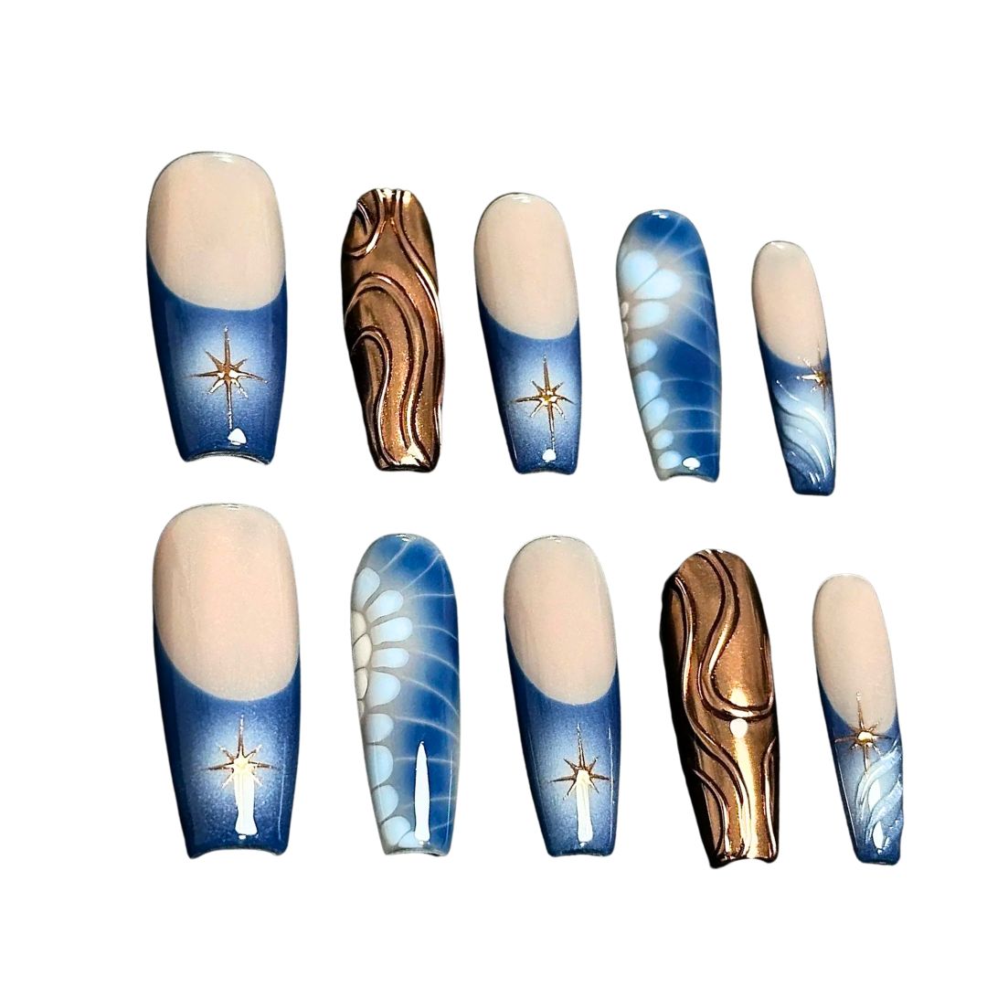 A press-on nail set with gradient blue bases, golden starburst designs, bronze wave patterns, and white floral accents, creating a celestial and elegant aesthetic.