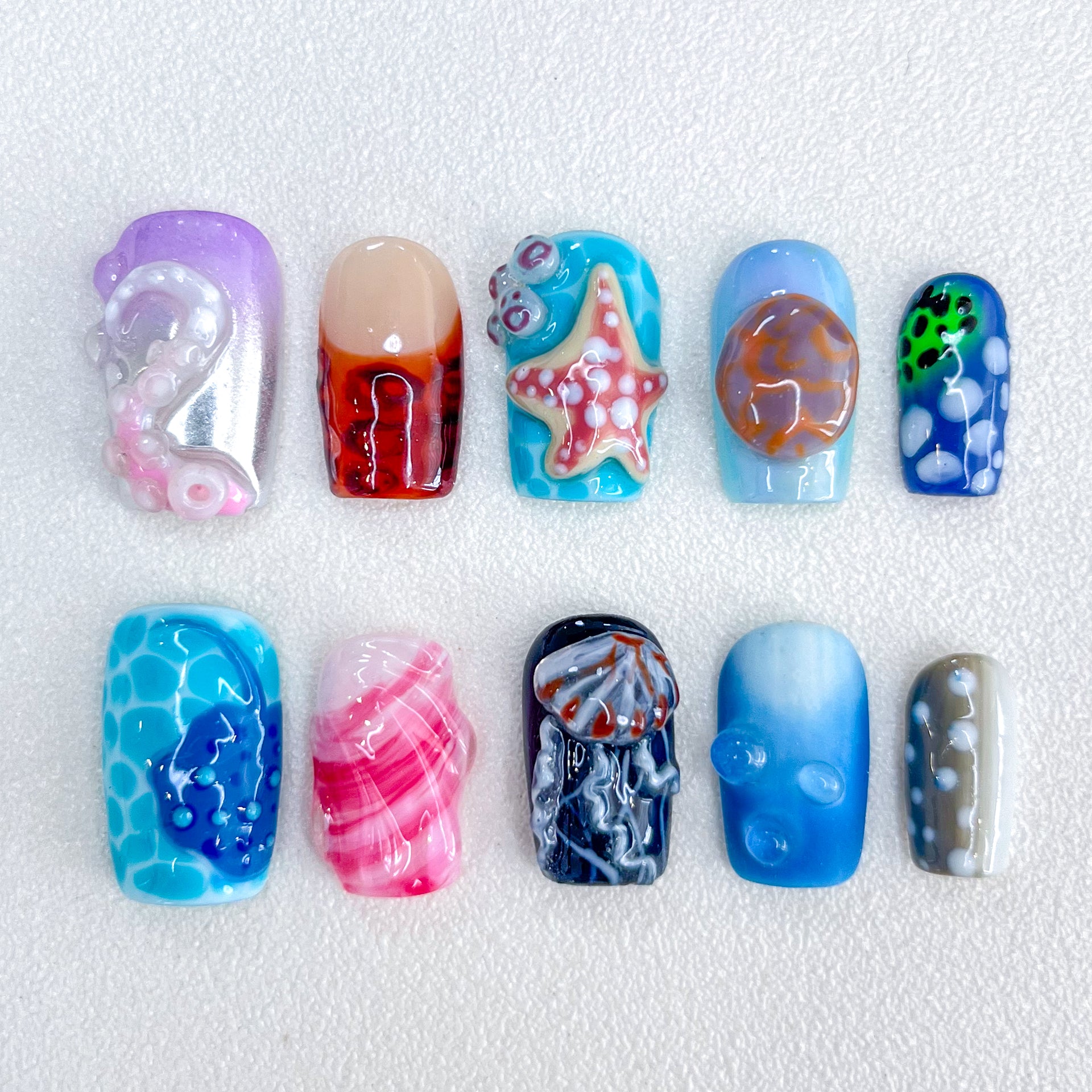 Marine Fantasy press-on nails with jellyfish, starfish, and coral designs in vibrant blues and reds, bringing a touch of marine magic to your nails.