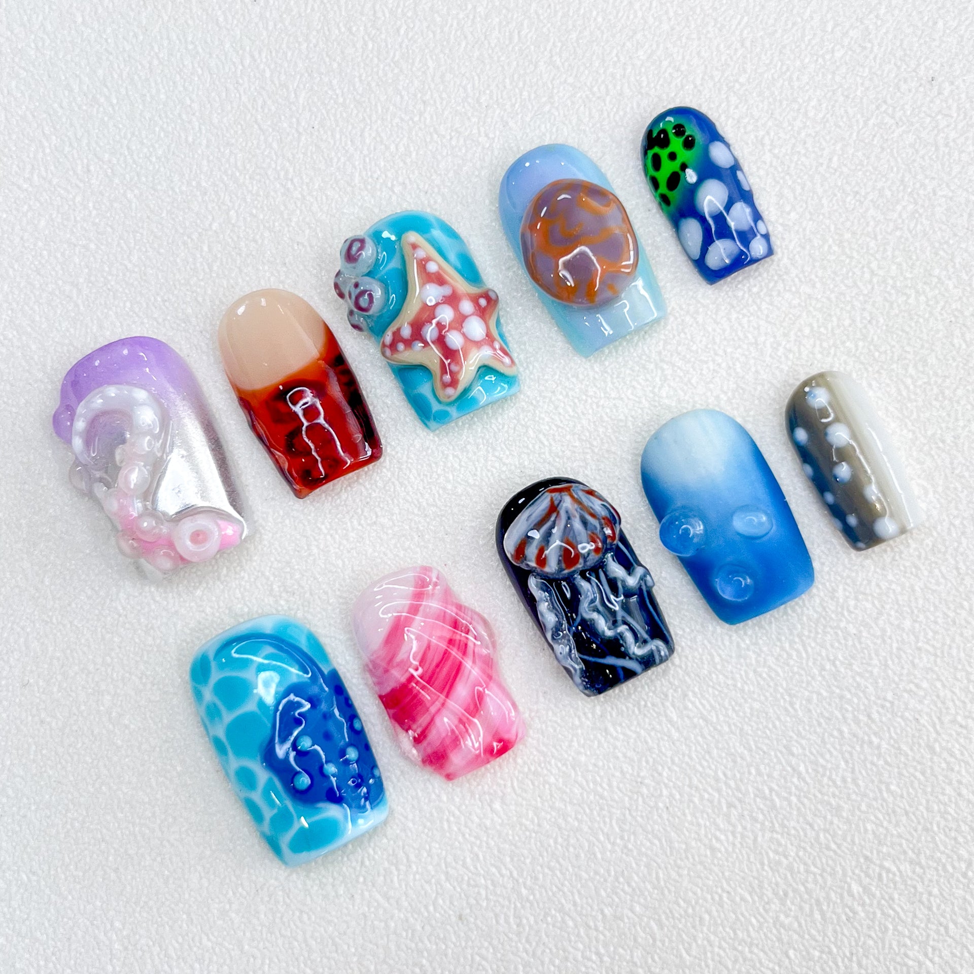 Marine Fantasy press-on nails with jellyfish, starfish, and coral designs in vibrant blues and reds, bringing a touch of marine magic to your nails.