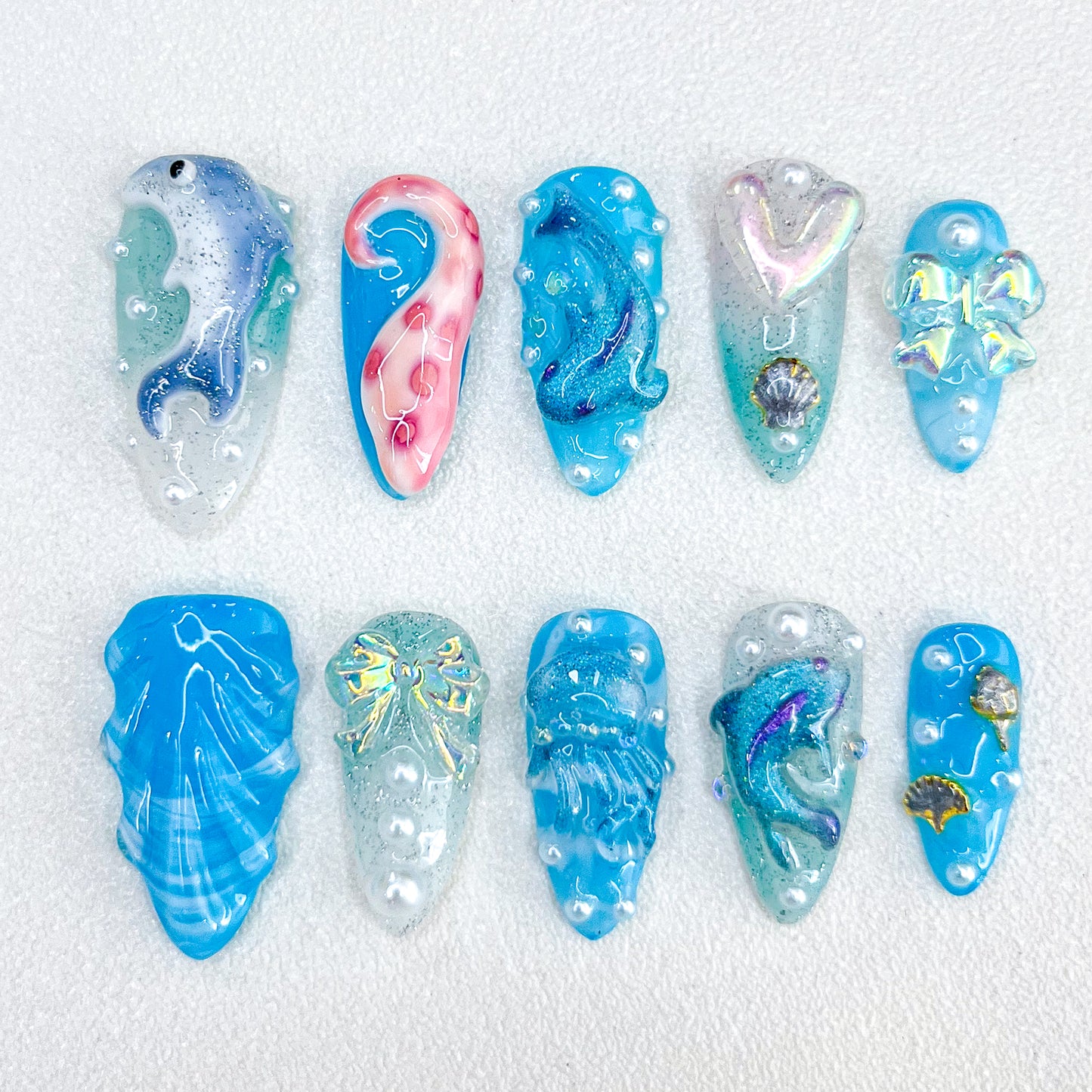 Dolphin Dreams press-on nails with dolphins, pearls, and ocean-inspired patterns in glittery blue hues for a lively aquatic style.