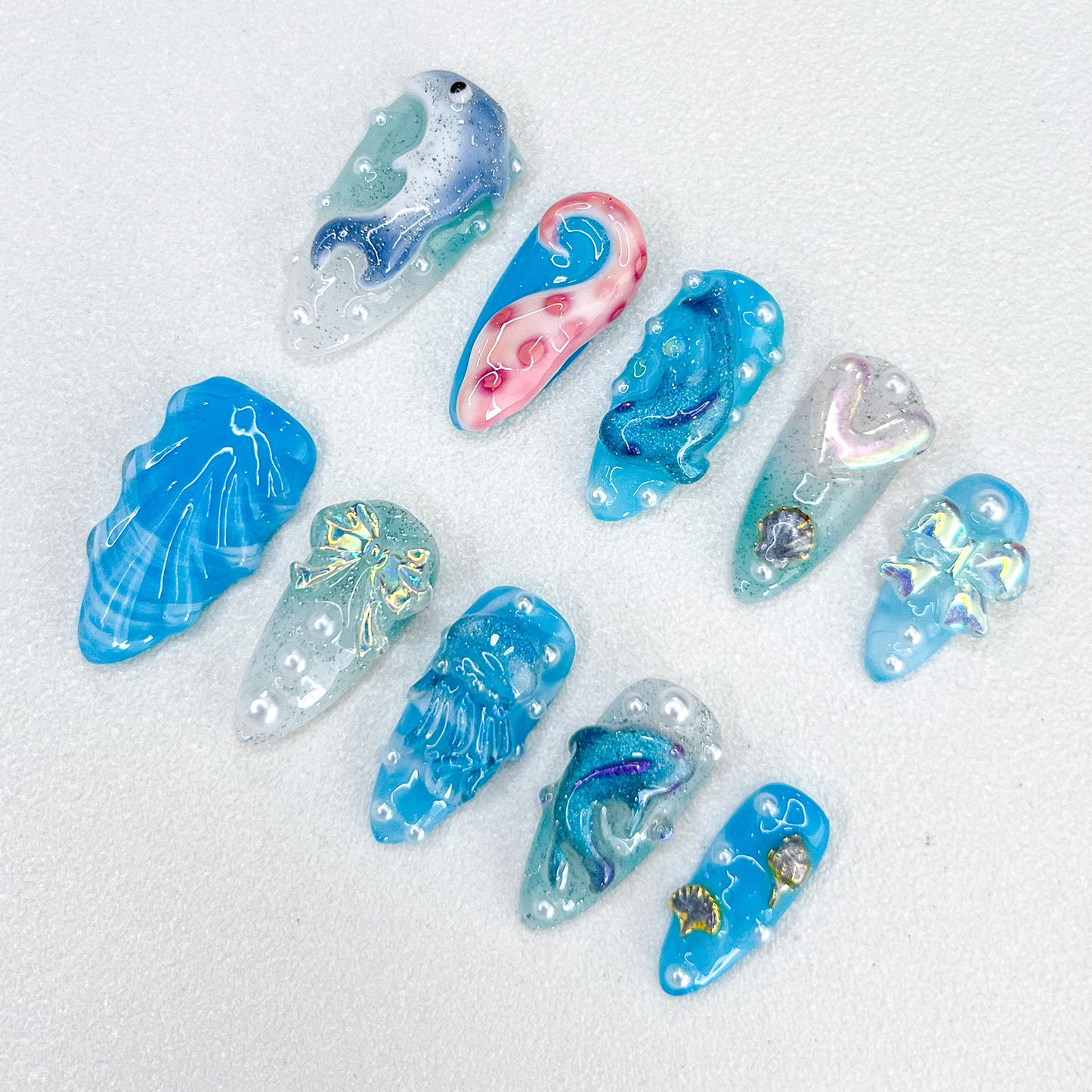 Dolphin Dreams press-on nails with dolphins, pearls, and ocean-inspired patterns in glittery blue hues for a lively aquatic style.