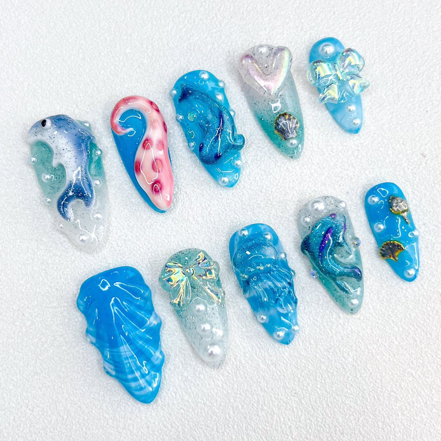 Dolphin Dreams press-on nails with dolphins, pearls, and ocean-inspired patterns in glittery blue hues for a lively aquatic style.