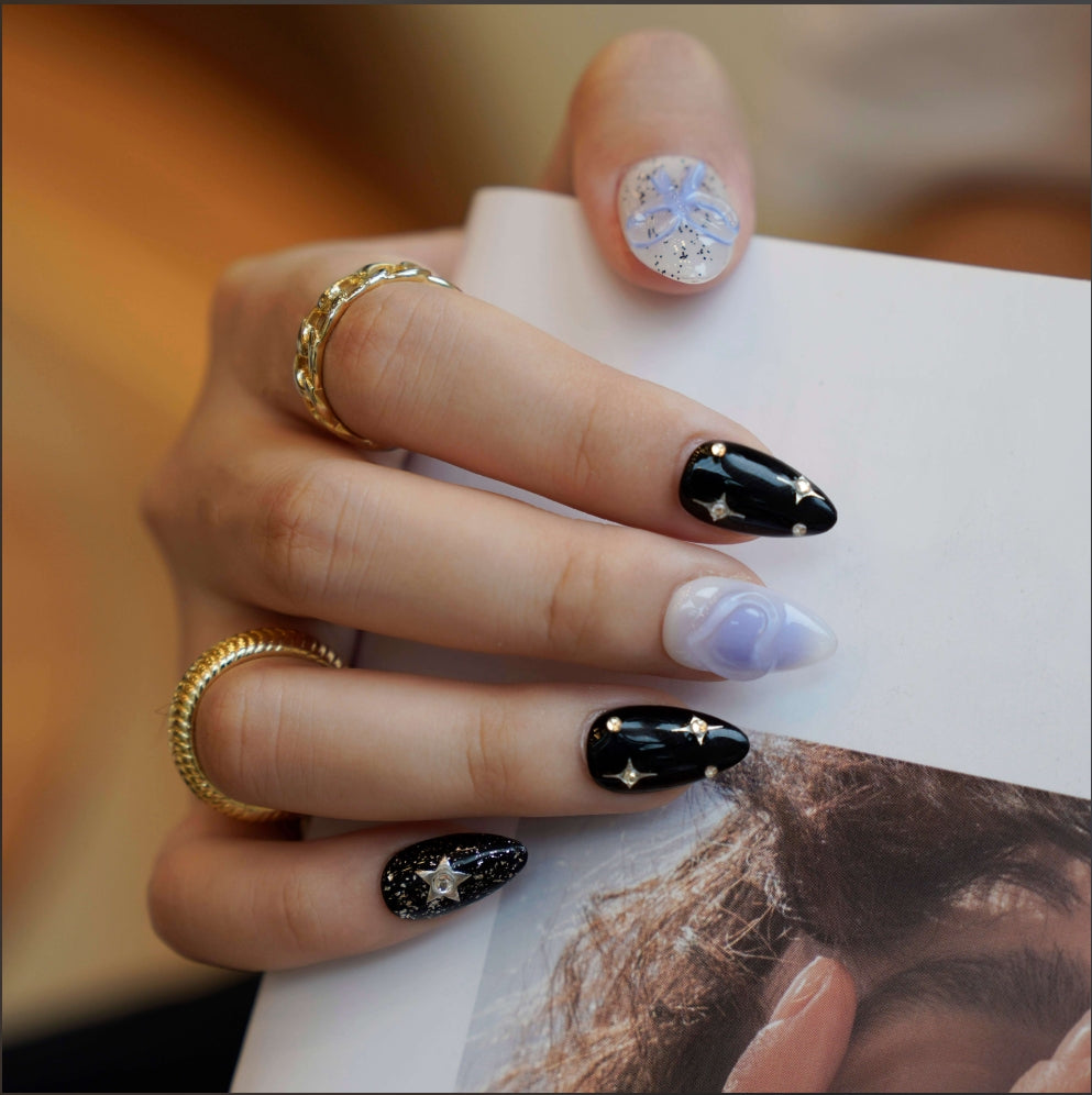 A cosmic-themed press-on nail set with a combination of black and pastel blue nails. The black nails feature glittery silver stars and rhinestones, while the blue nails include elegant bow designs. Perfect for a celestial and dreamy style.