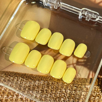 A set of bright yellow glossy press-on nails neatly arranged in a transparent case, featuring a vibrant and smooth finish, ideal for everyday wear, with a warm and natural backdrop.