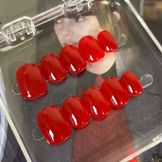 A set of vibrant red glossy press-on nails neatly placed in a transparent box, showcasing a smooth, luxurious finish, ideal for multiple occasions.