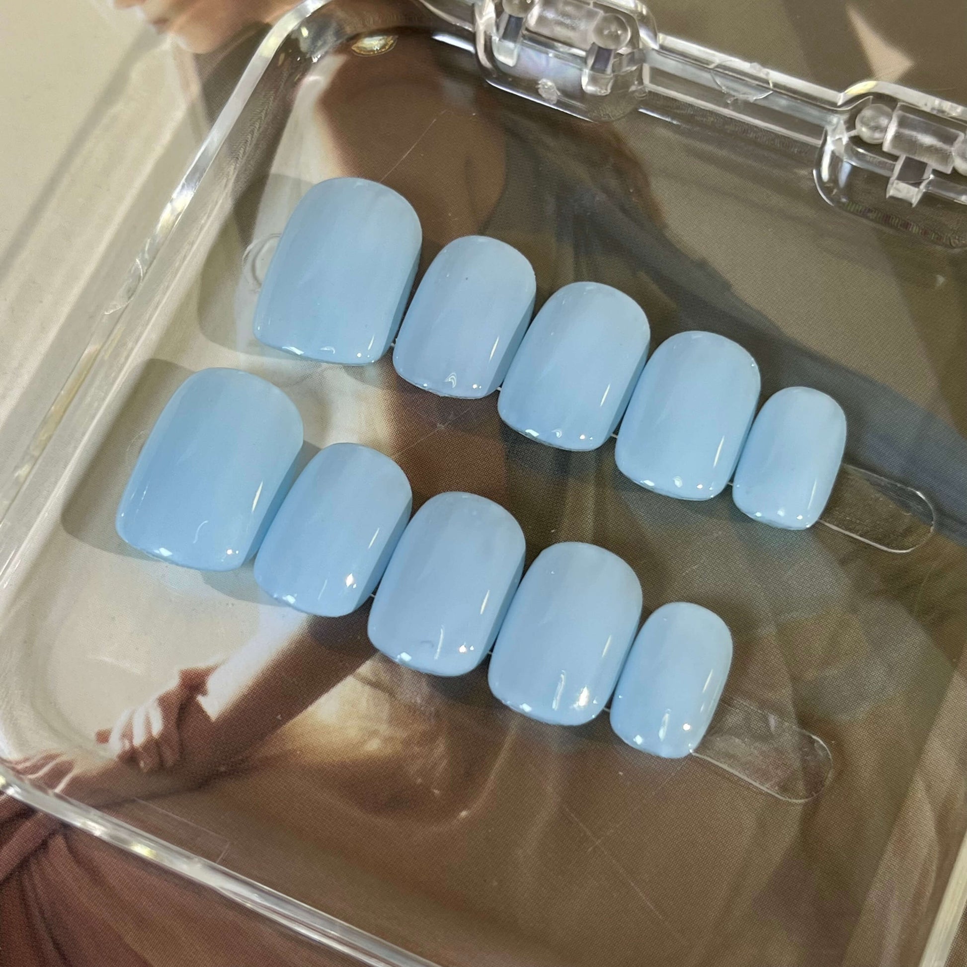 A set of light blue glossy press-on nails neatly arranged in a transparent case, featuring a natural, smooth finish, ideal for achieving a simple and elegant daily style.