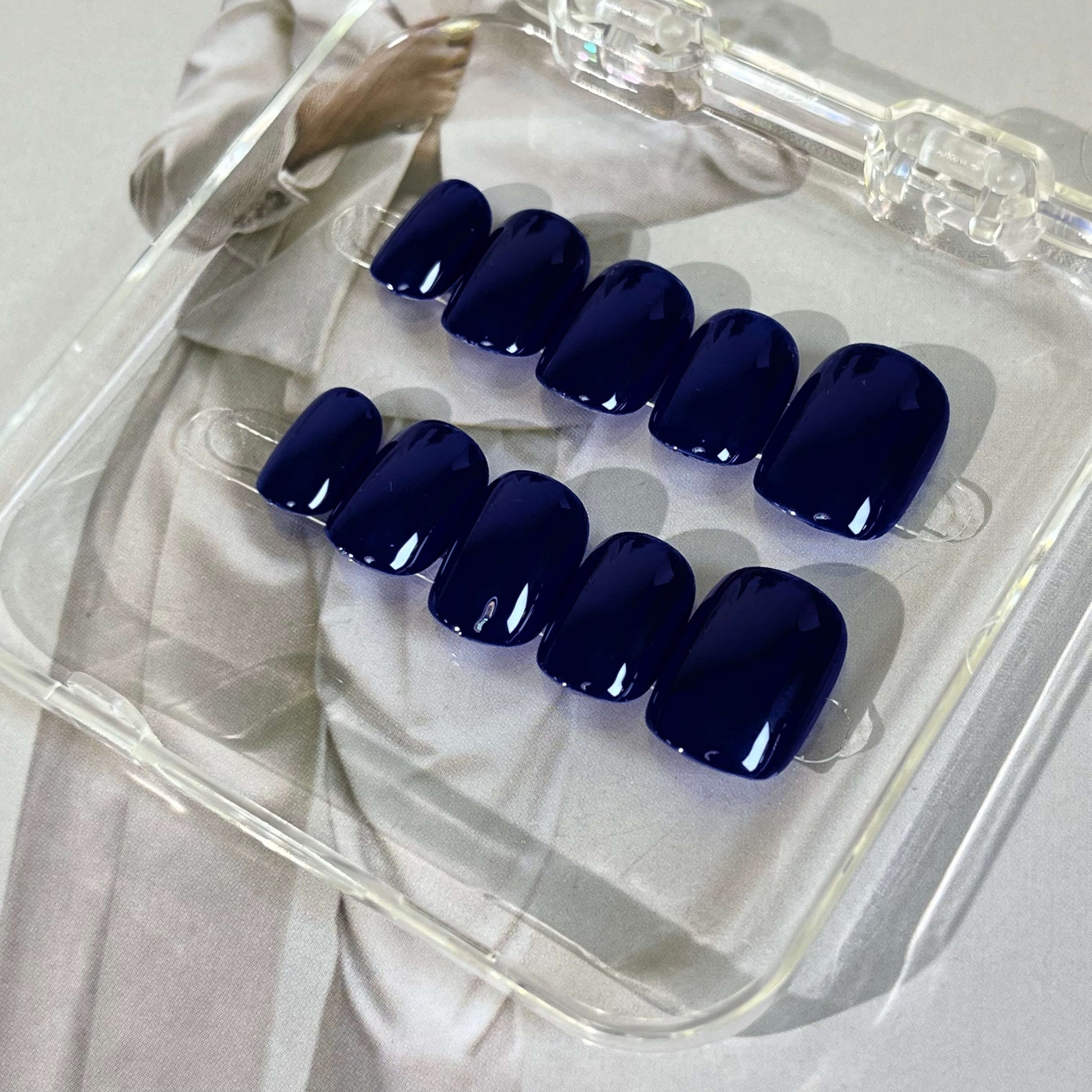 A set of deep blue glossy press - on nails neatly arranged in a transparent case, featuring a luxurious and smooth finish, ideal for formal or evening wear, with a deep and captivating color.