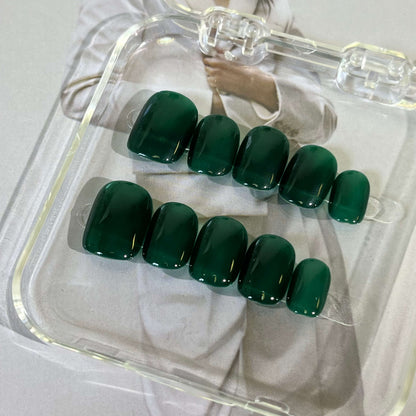 A set of dark green glossy press - on nails neatly placed in a transparent box, showcasing a rich, smooth finish, ideal for outdoor or nature - related events.