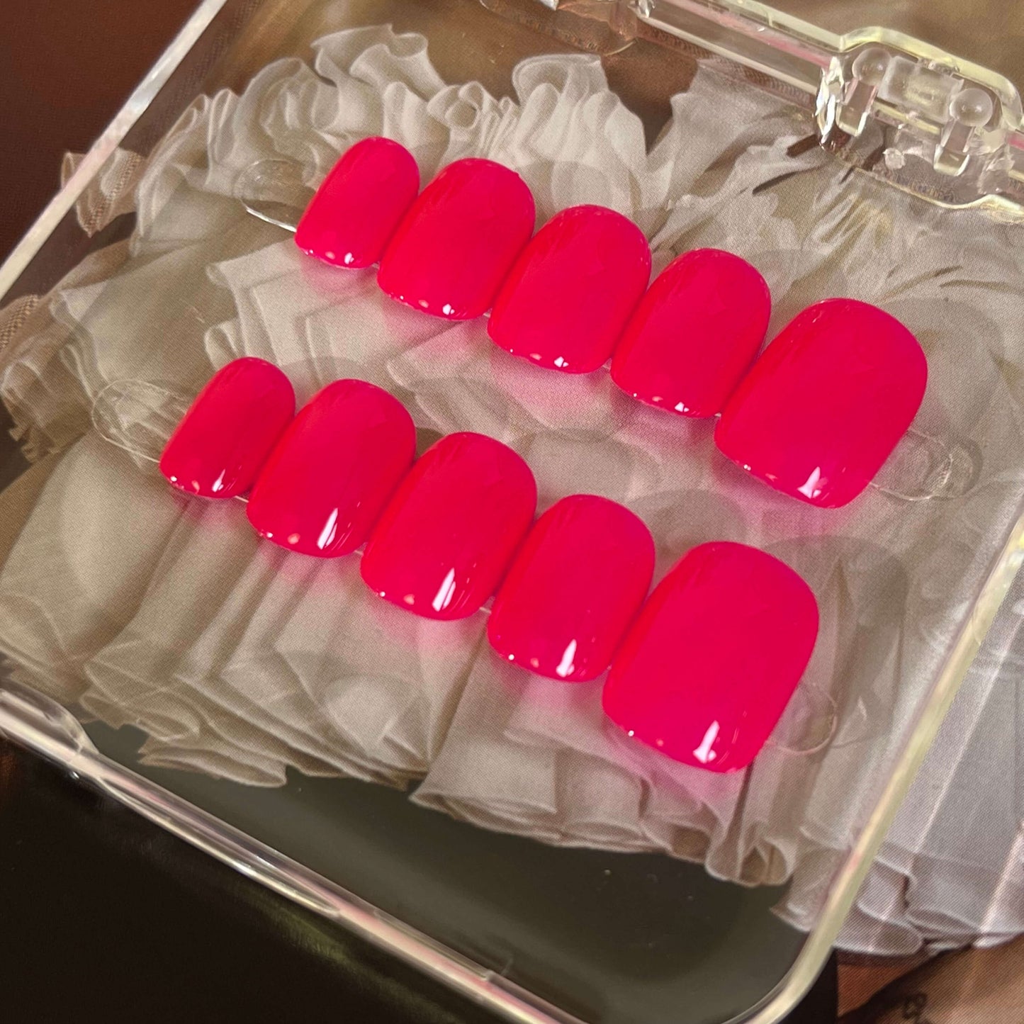 A set of bright red glossy press - on nails neatly arranged in a transparent case, featuring a vivid, smooth finish, ideal for festive or romantic occasions.