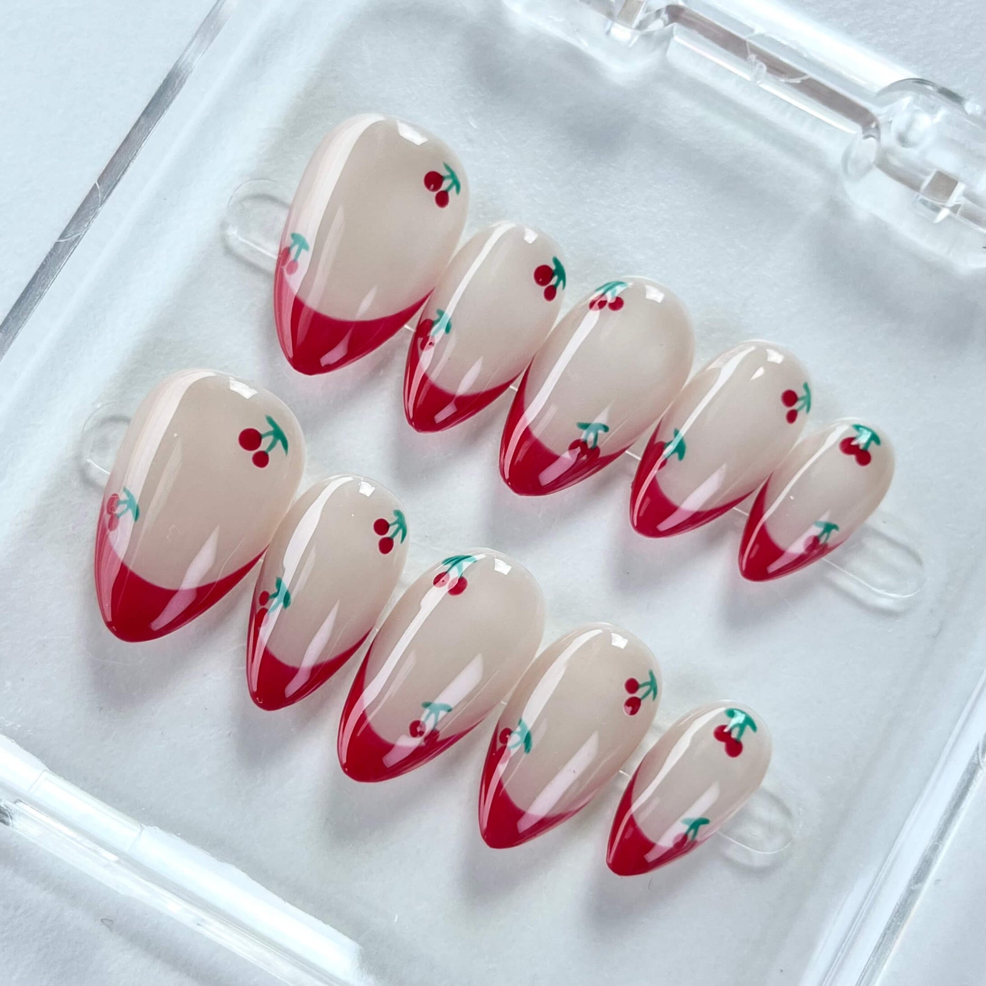 A cheerful nail design named "Cherry Delight," featuring nude nails with crisp white French tips, accented by tiny red cherries with green stems. This set captures the essence of a sunlit cherry orchard, bringing a splash of fresh energy to any look.